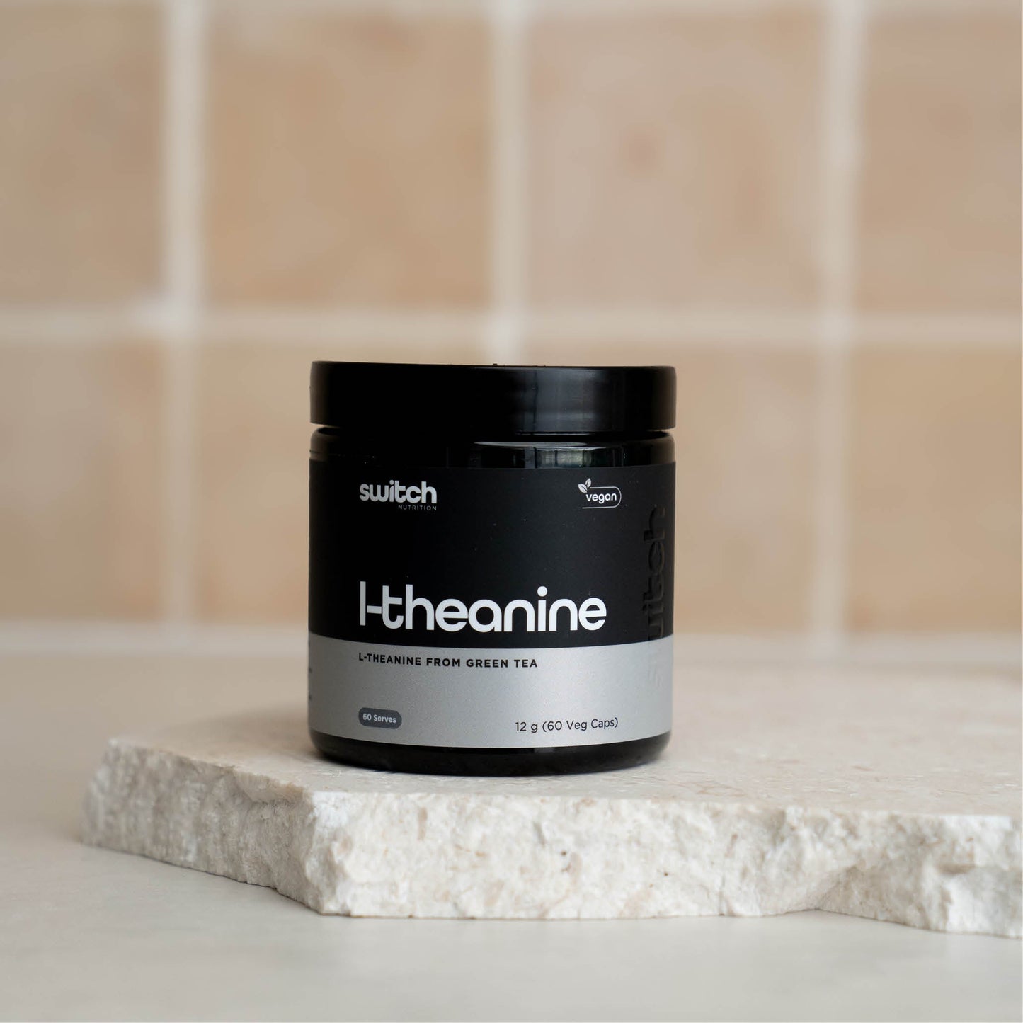 A container of Switch Nutrition L-Theanine supplement placed on a light-colored stone surface, with a tiled background.