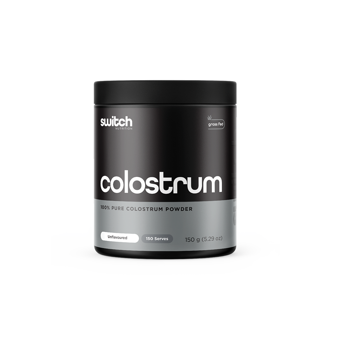 A container of Switch Nutrition's Colostrum, labeled as 100% pure colostrum powder from grass-fed sources. The packaging is black with white and grey text, indicating it's unflavoured with 150 servings in a 150g container.