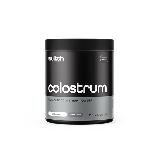 A container of Switch Nutrition's Colostrum, labeled as 100% pure colostrum powder from grass-fed sources. The packaging is black with white and grey text, indicating it's unflavoured with 150 servings in a 150g container.