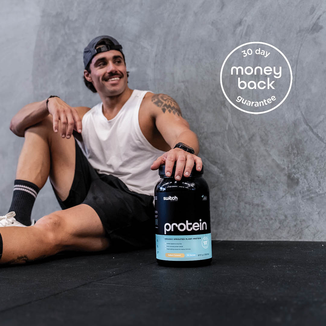 Male in gym sitting on the floor with a Protein Switch tub, with a '30-day money back guarantee' badge.